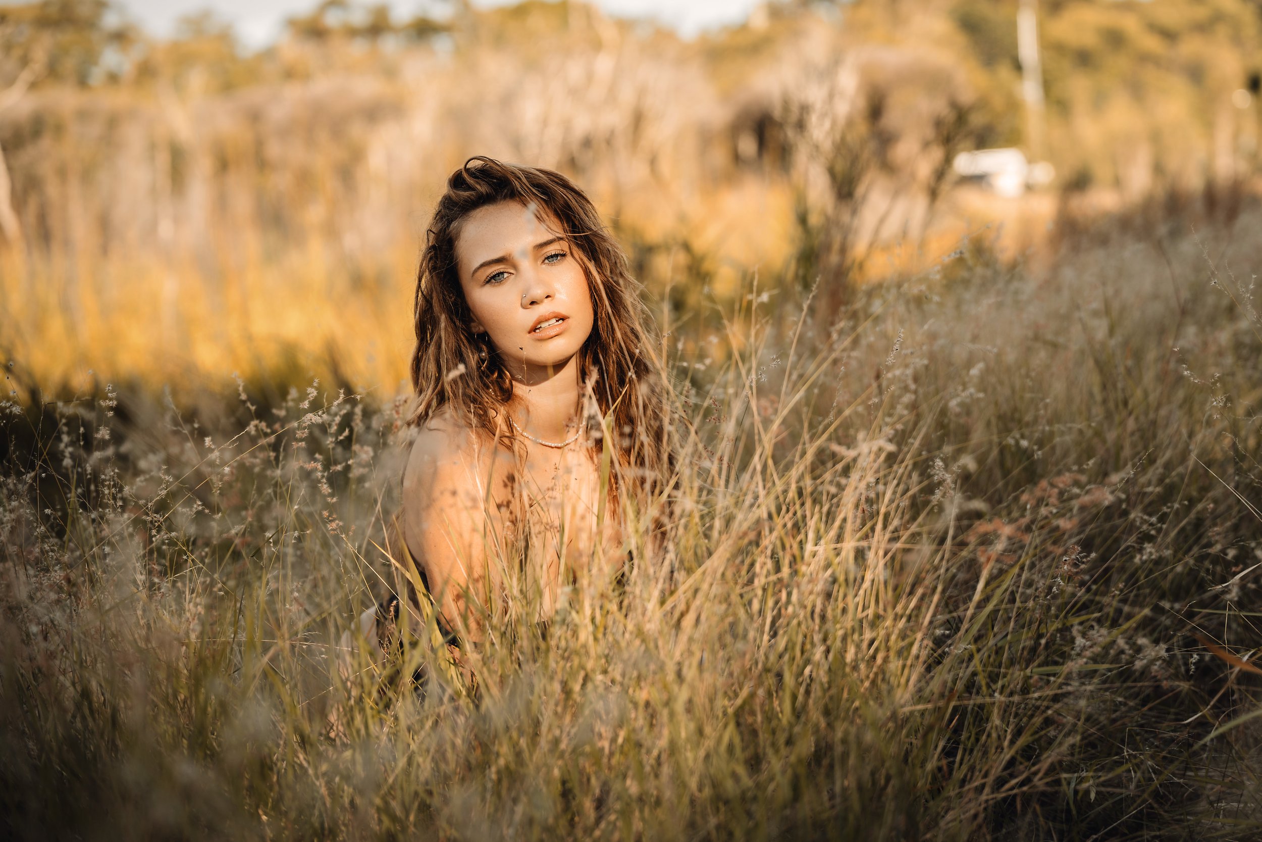 Woman sitting in tall golden grass at sunset, looking at the camera